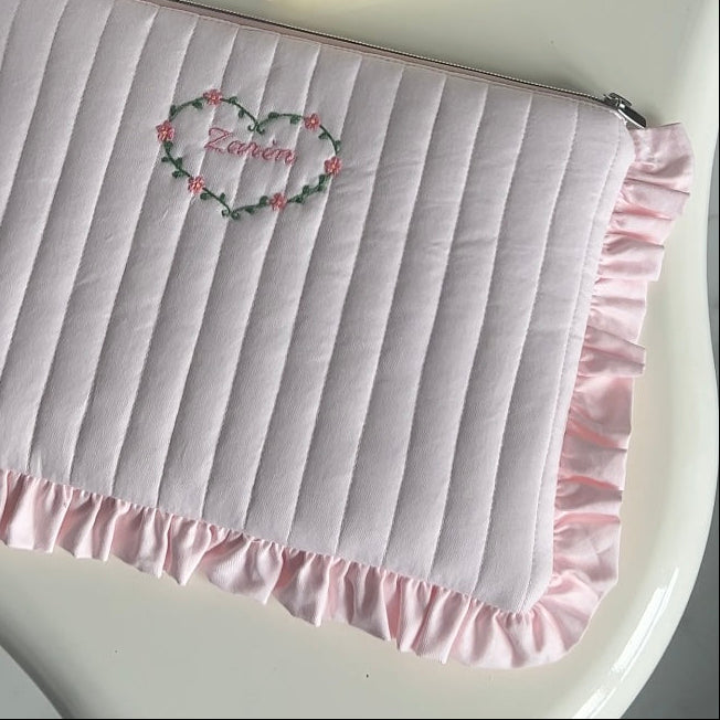 Pink pouch with ruffled edge and embroidered name on a white background